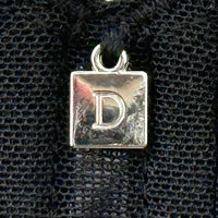 Close-up of Dominique Mallory Bra charm detail with silver 'D' logo on black mesh fabric for a stylish finish.