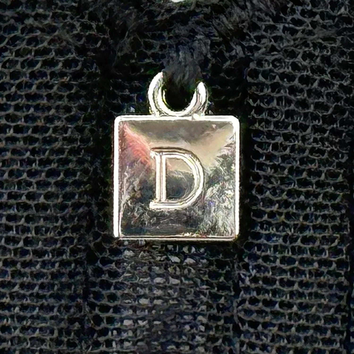 Close-up of Dominique Mallory Bra charm detail with silver 'D' logo on black mesh fabric for a stylish finish.