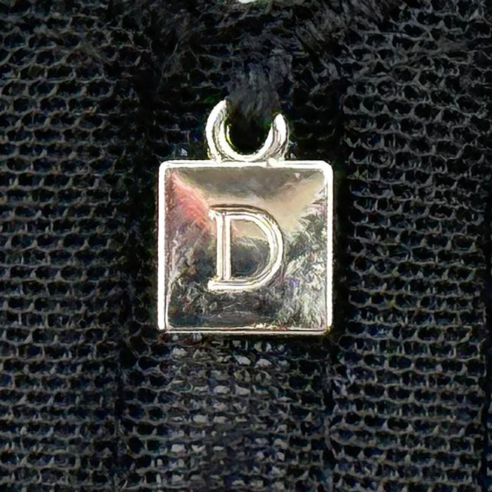 Close-up of Dominique Mallory Bra charm detail with silver 'D' logo on black mesh fabric for a stylish finish.