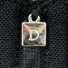 Close-up of Dominique Mallory Bra charm detail with silver 'D' logo on black mesh fabric for a stylish finish.