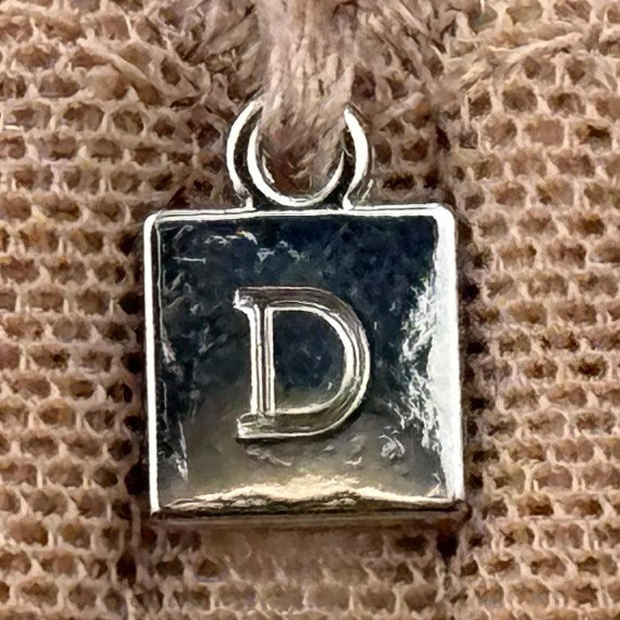 Close-up of Dominique Mallory bra charm with engraved 'D' logo, attached to center gore of the mocha minimizer bra.