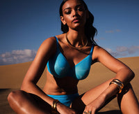 Model wearing Gossard Glossies Sheer Bra Atomic Blue in a desert setting, showcasing its lightweight, seamless plunge design and bold blue color.