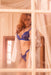 Model poses in sapphire Midnight Amour Eyelash Lace Bra Set behind a window, showcasing sheer lace and scalloped panty design.