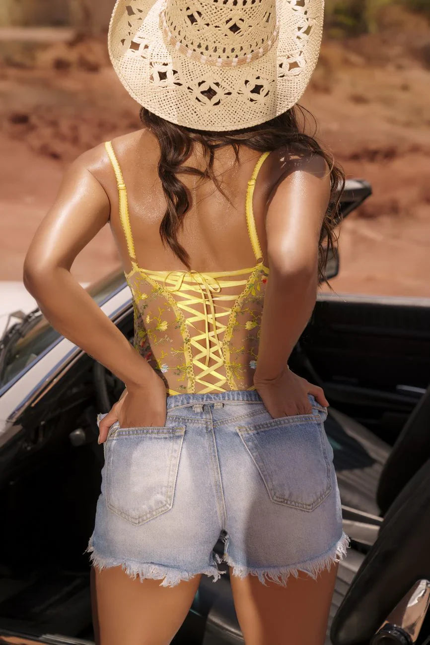 Sheer Mesh Bodysuit Mapale Daisy Bliss in yellow with lace-up back detail, styled with denim shorts. Sexy floral lingerie bodysuit for summer looks.